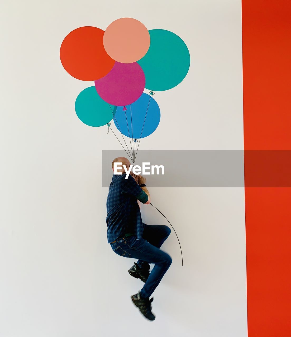 Digital composite image of man holding balloons against wall