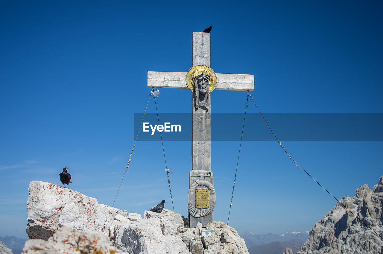 Low angle view of cross on rock against clear blue sky