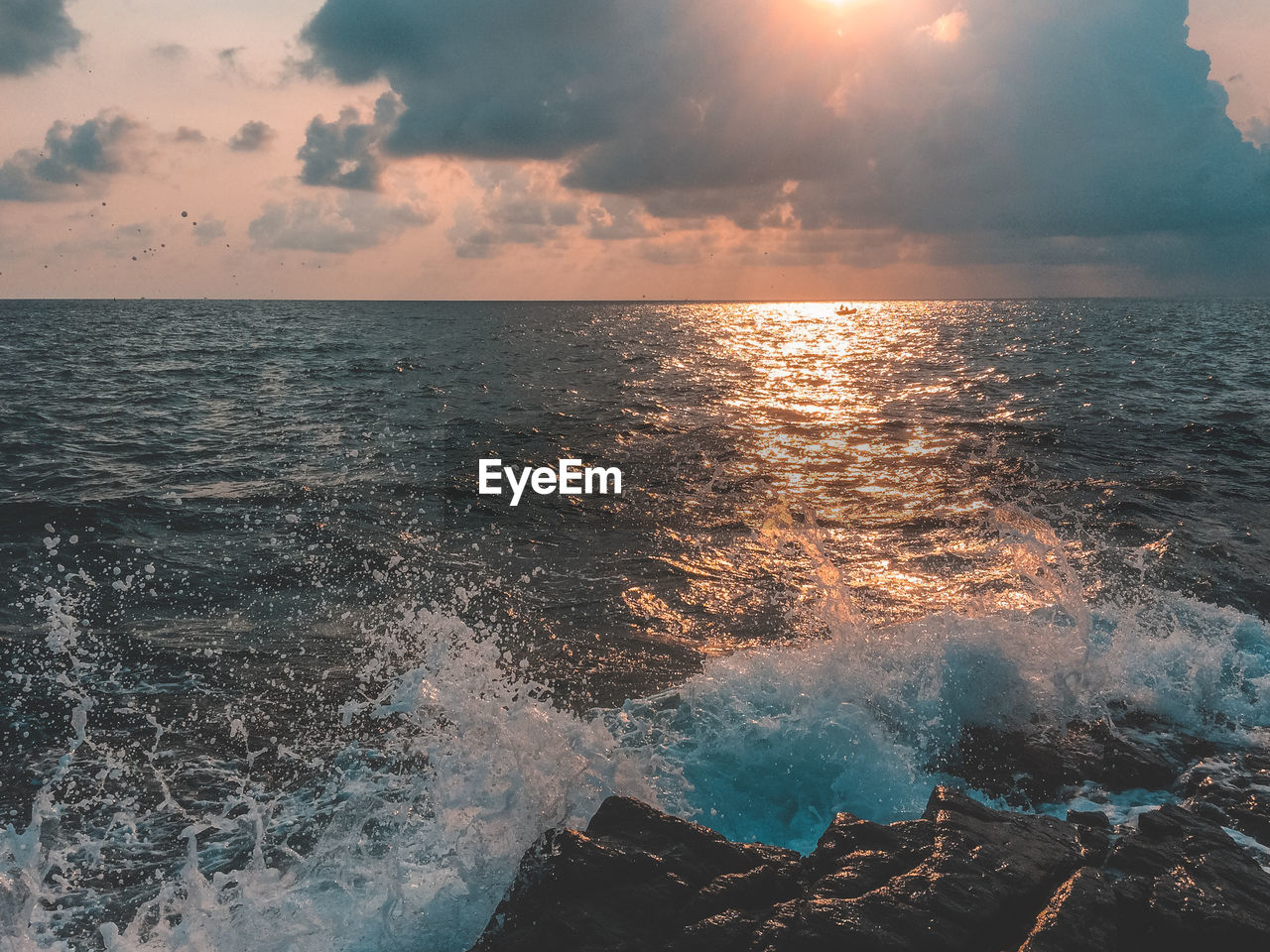 Splashing water of sea against sky during sunset