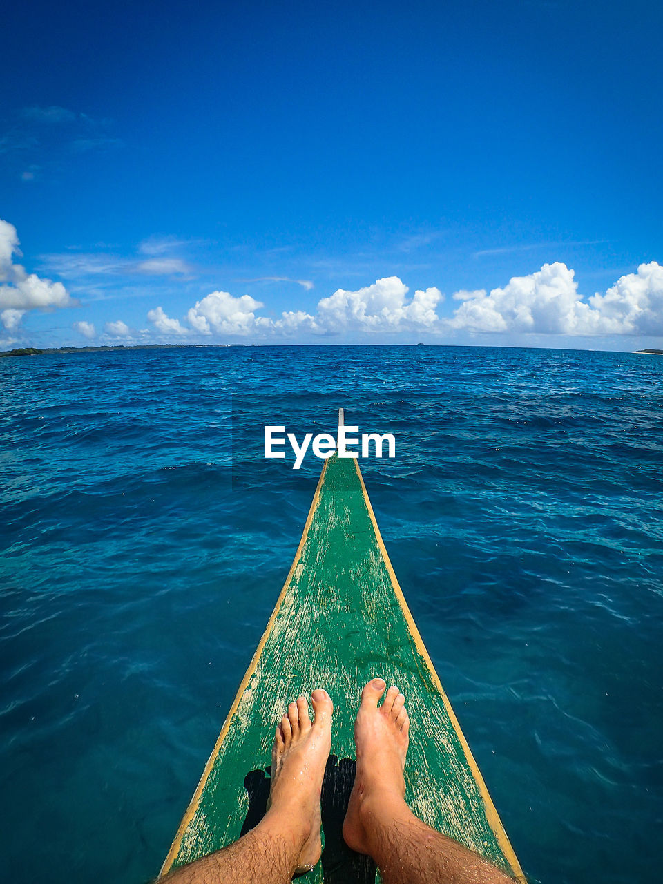 Low section of man sitting on boat in sea against blue sky