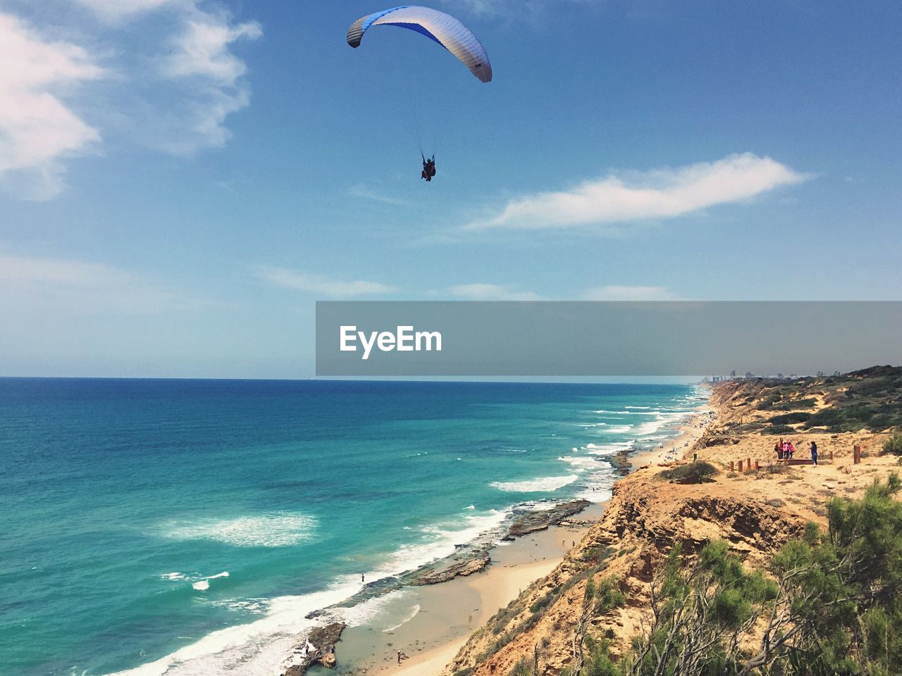 Person paragliding over beach against sky