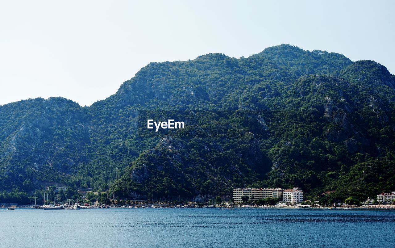 Scenic view of sea by mountain against clear sky