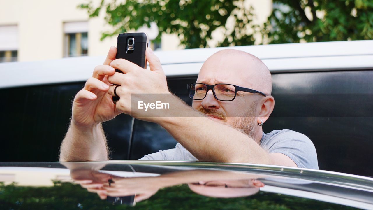 Close-up of man wearing eyeglasses using mobile phone by car