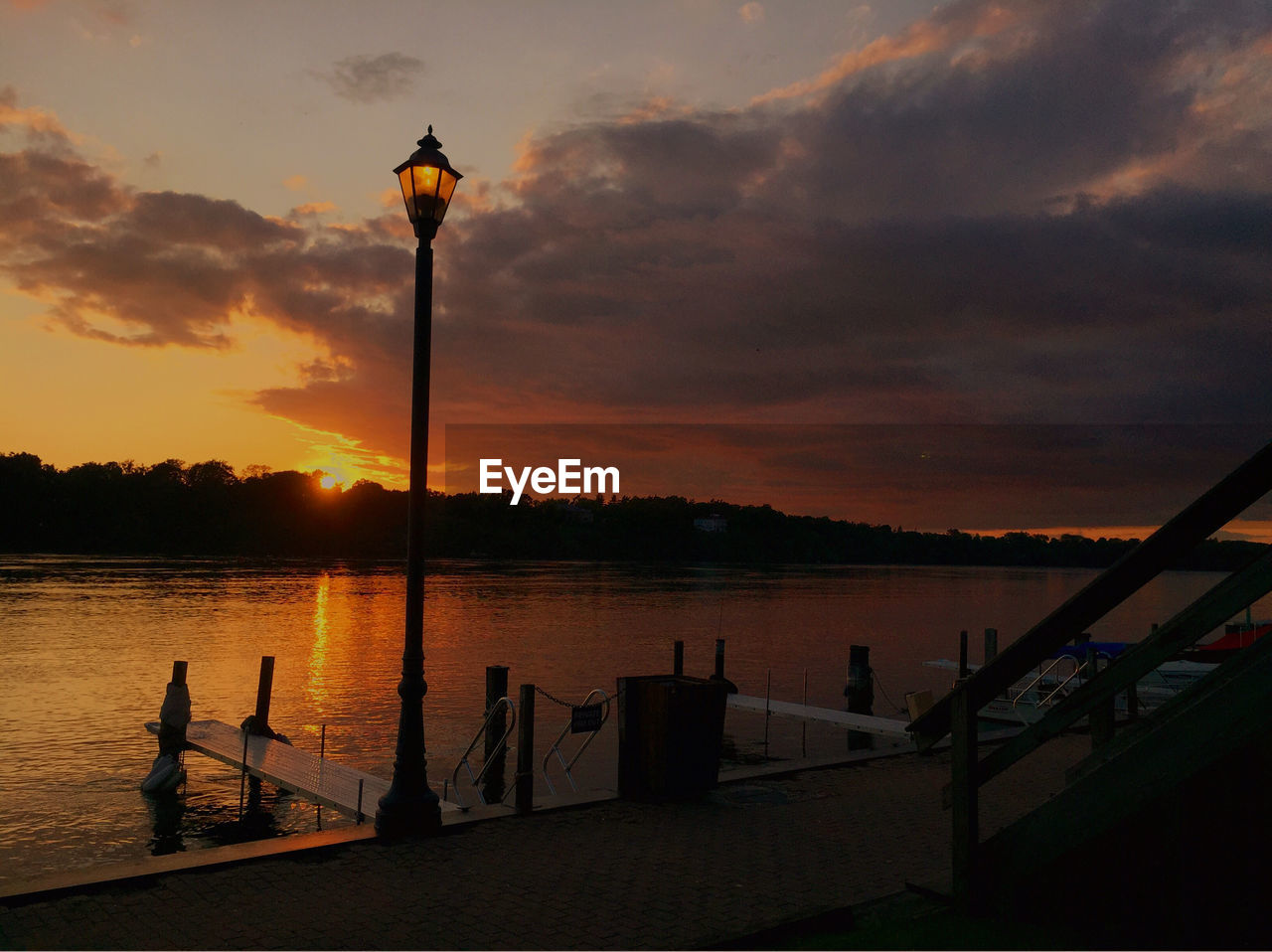 SILHOUETTE STREET LIGHTS BY LAKE AGAINST SKY DURING SUNSET