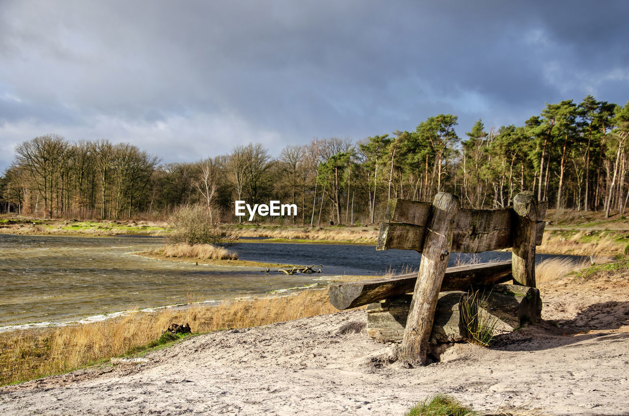 Wooden bench on a sandy beach by a lake under sunny, yet cold and windy weather circumstances