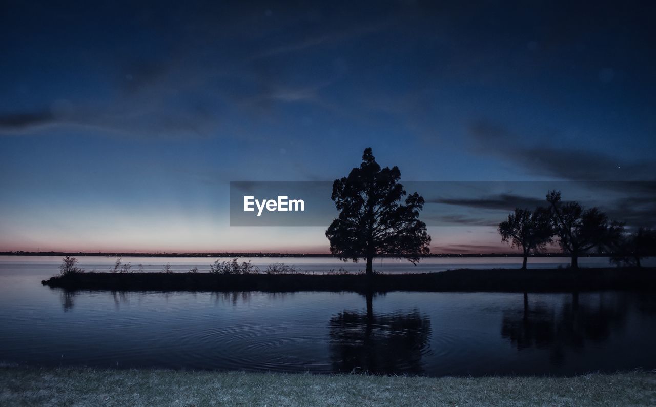 Silhouette trees by lake against sky during sunset