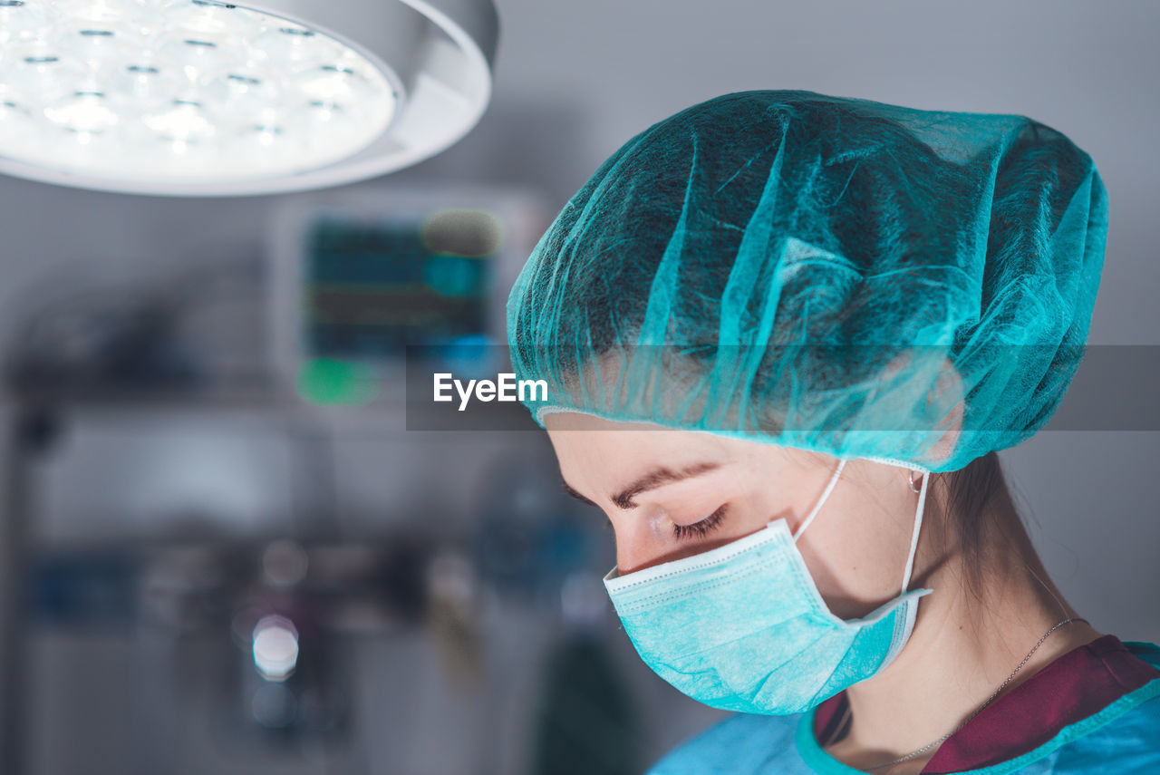 Side view of adult woman in medical mask and hat performing surgery in hospital