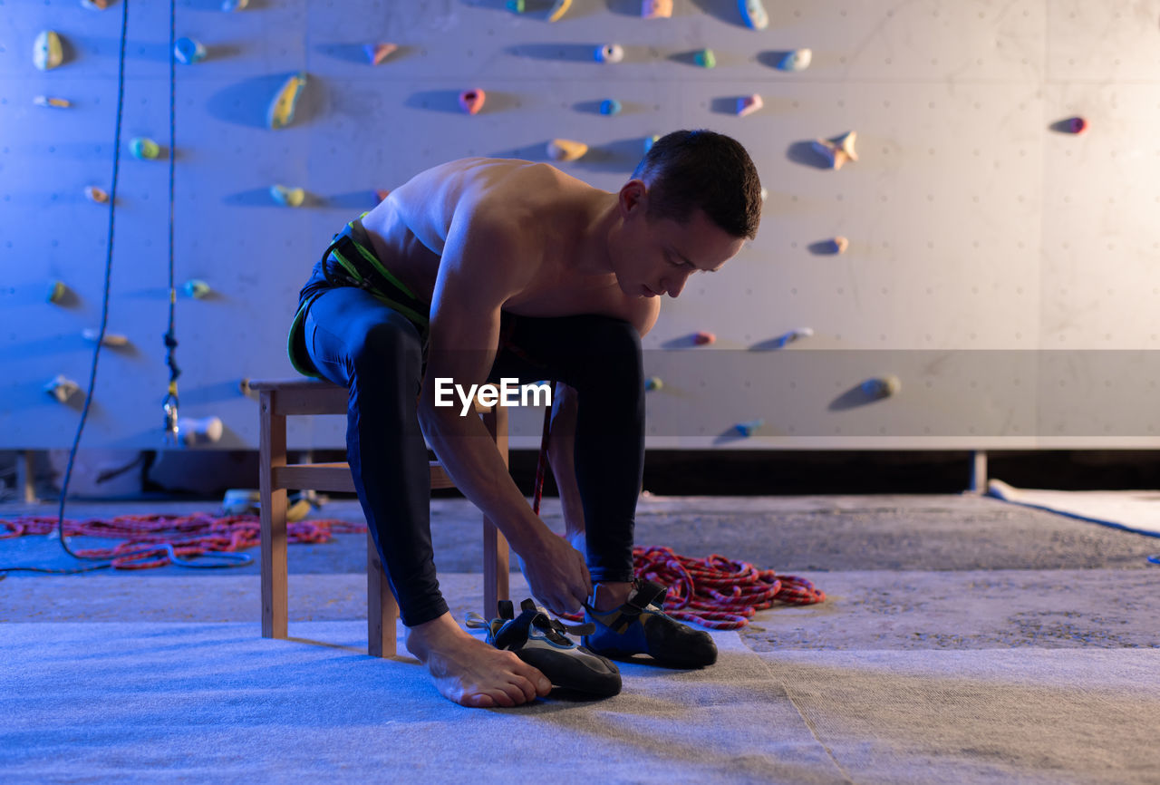 Young climber putting on shoes near wall