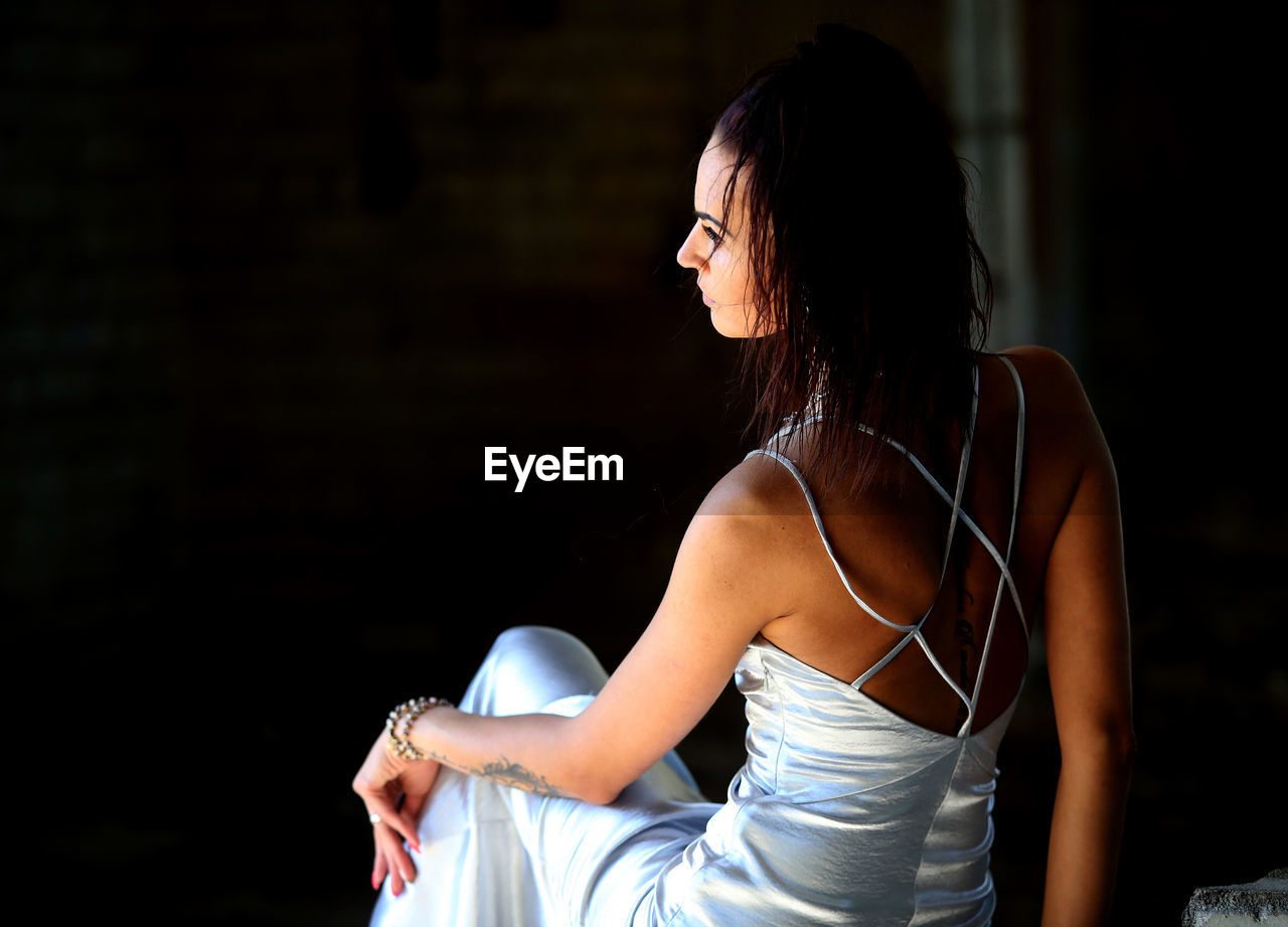 Rear view of mid adult woman in dress looking away while sitting outdoors at night