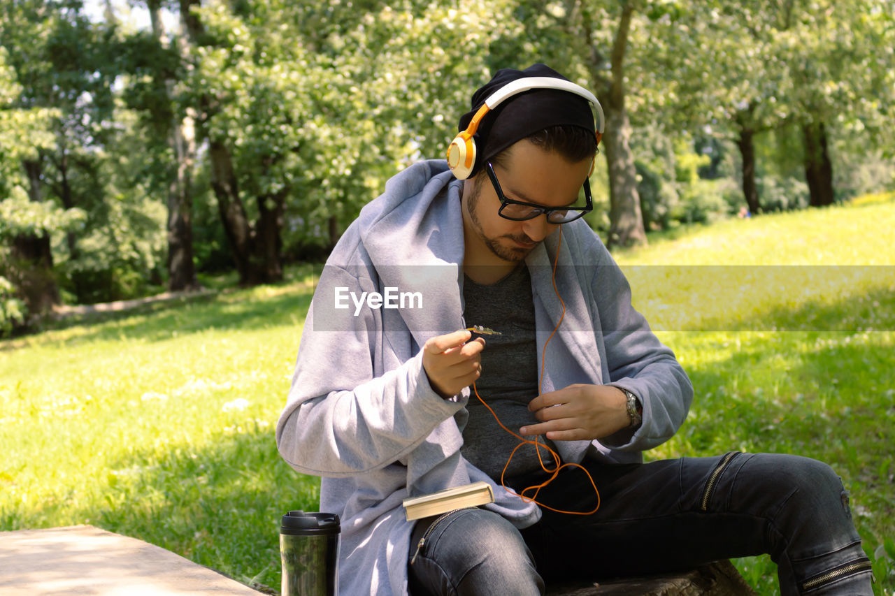 Casual man adjusting headphones while spending spring day in nature.