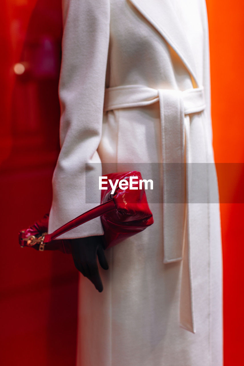 Fancy details of a classic white long coat with a belt and a patent red handbag. women's fashion