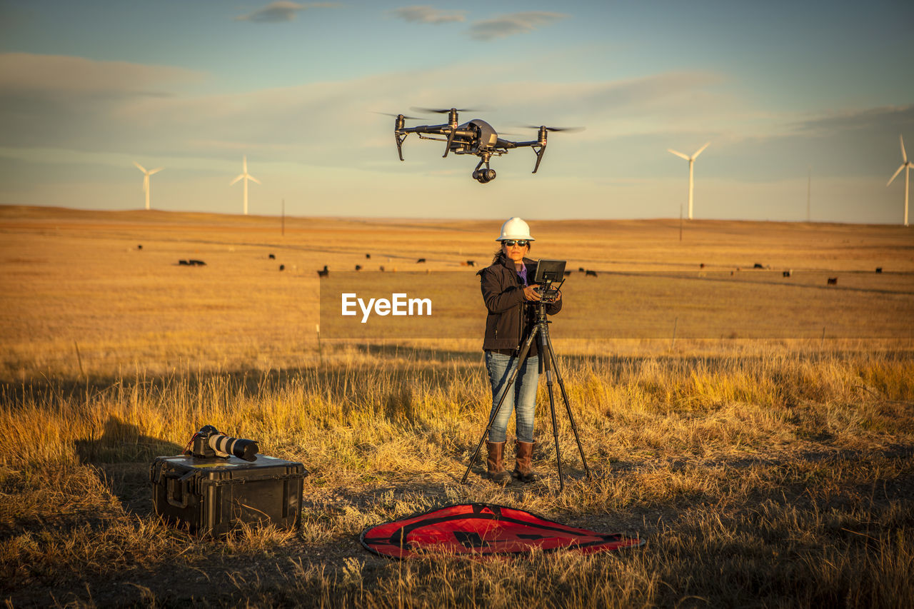 Female drone pilot flies in a wind farm at sunrise