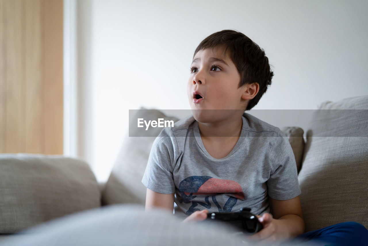 Boy playing video game while sitting on sofa at home