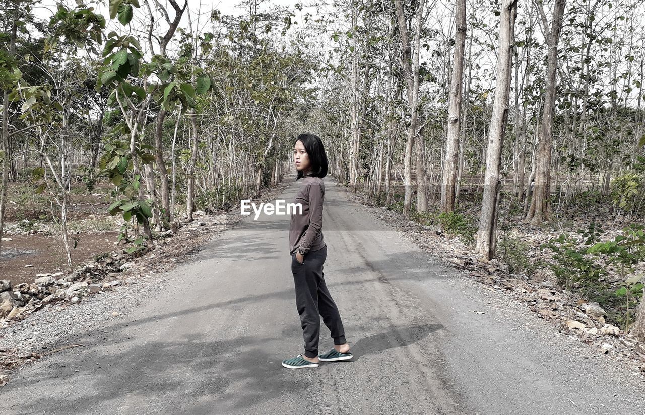 Full length of woman standing on road amidst trees