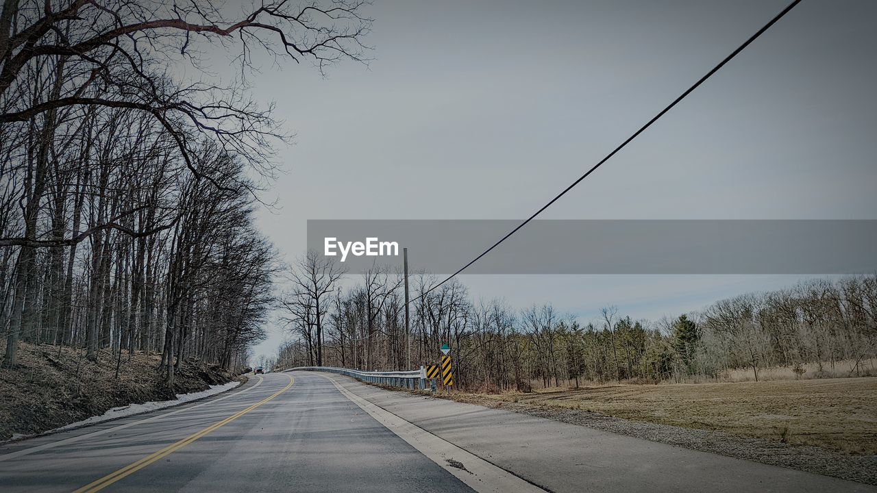 tree, road, transportation, the way forward, sky, plant, bare tree, nature, winter, diminishing perspective, no people, vanishing point, sign, morning, road marking, infrastructure, marking, highway, lane, day, empty road, outdoors, snow, scenics - nature, symbol, landscape, beauty in nature, tranquility, street, travel, city, environment, mode of transportation, land, tranquil scene, country road, cold temperature