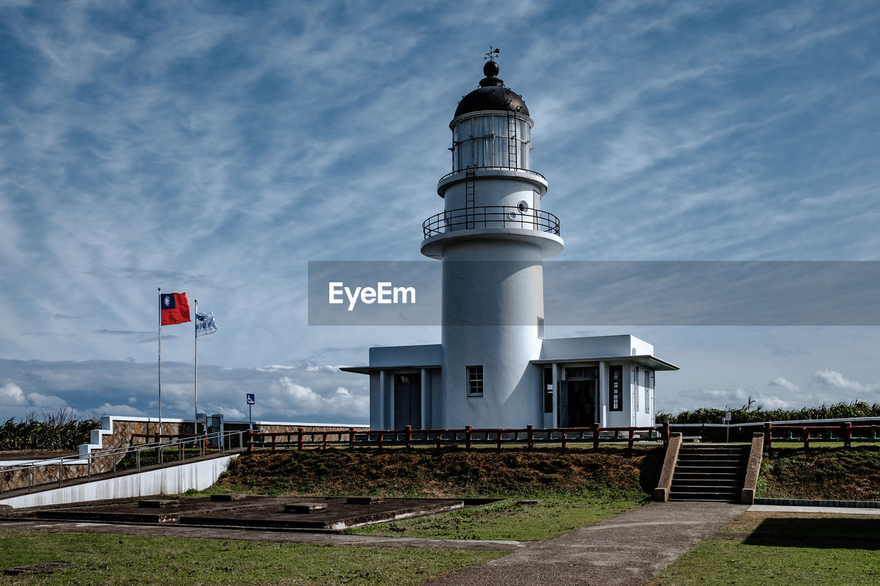 Lighthouse by building against sky