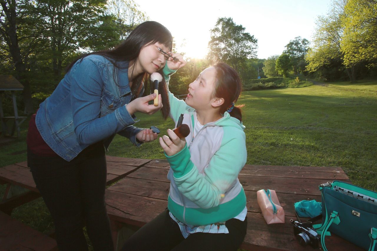 Young woman applying mascara to friend outdoors