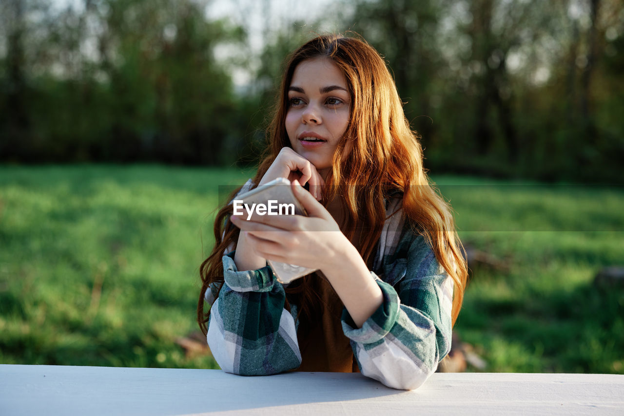 young woman using mobile phone while sitting on field