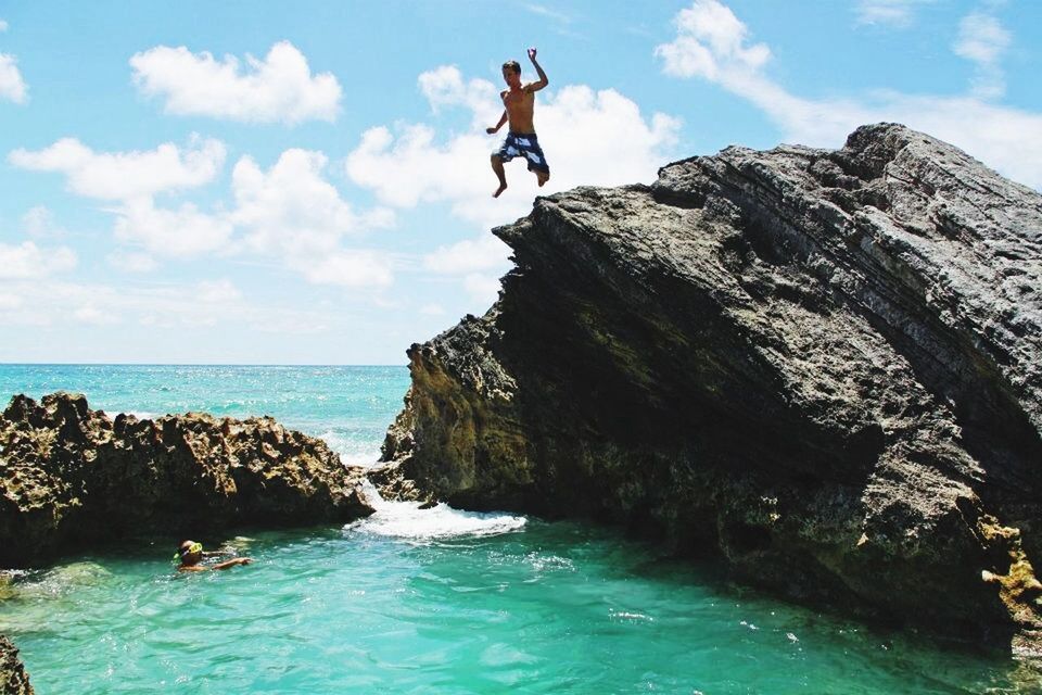 Full length of man jumping into sea from rock against sky