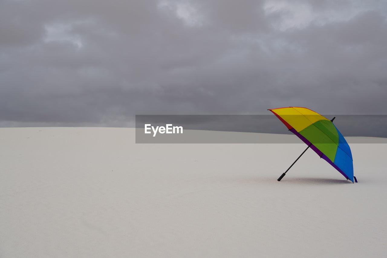 cloud, sky, wind, windsports, nature, environment, sports, toy, storm, land, overcast, kite - toy, kite sports, umbrella, sport kite, sand, storm cloud, copy space, water, beauty in nature, beach, no people, sea, tranquility, multi colored, day, outdoors, scenics - nature, horizon, protection, wing, vacation, tranquil scene, leisure activity, trip, holiday