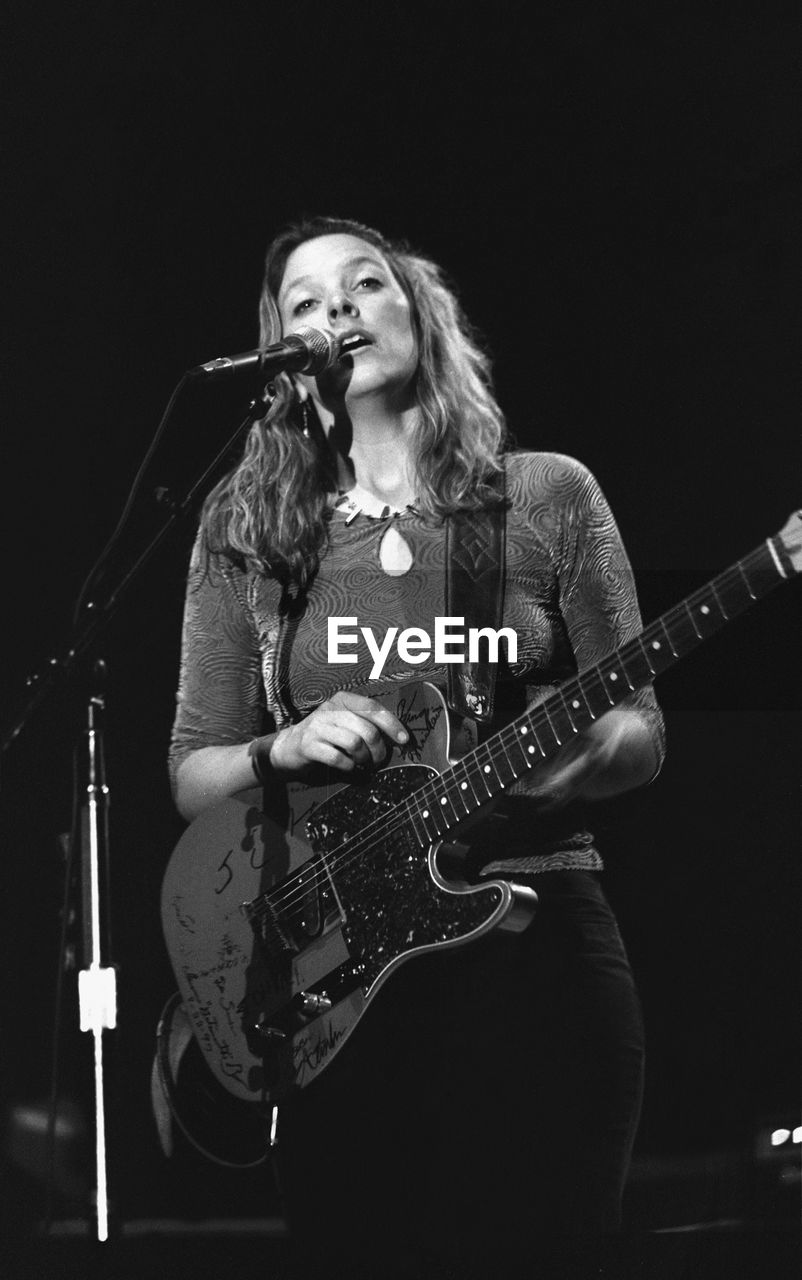 YOUNG WOMAN PLAYING GUITAR AT CAMERA