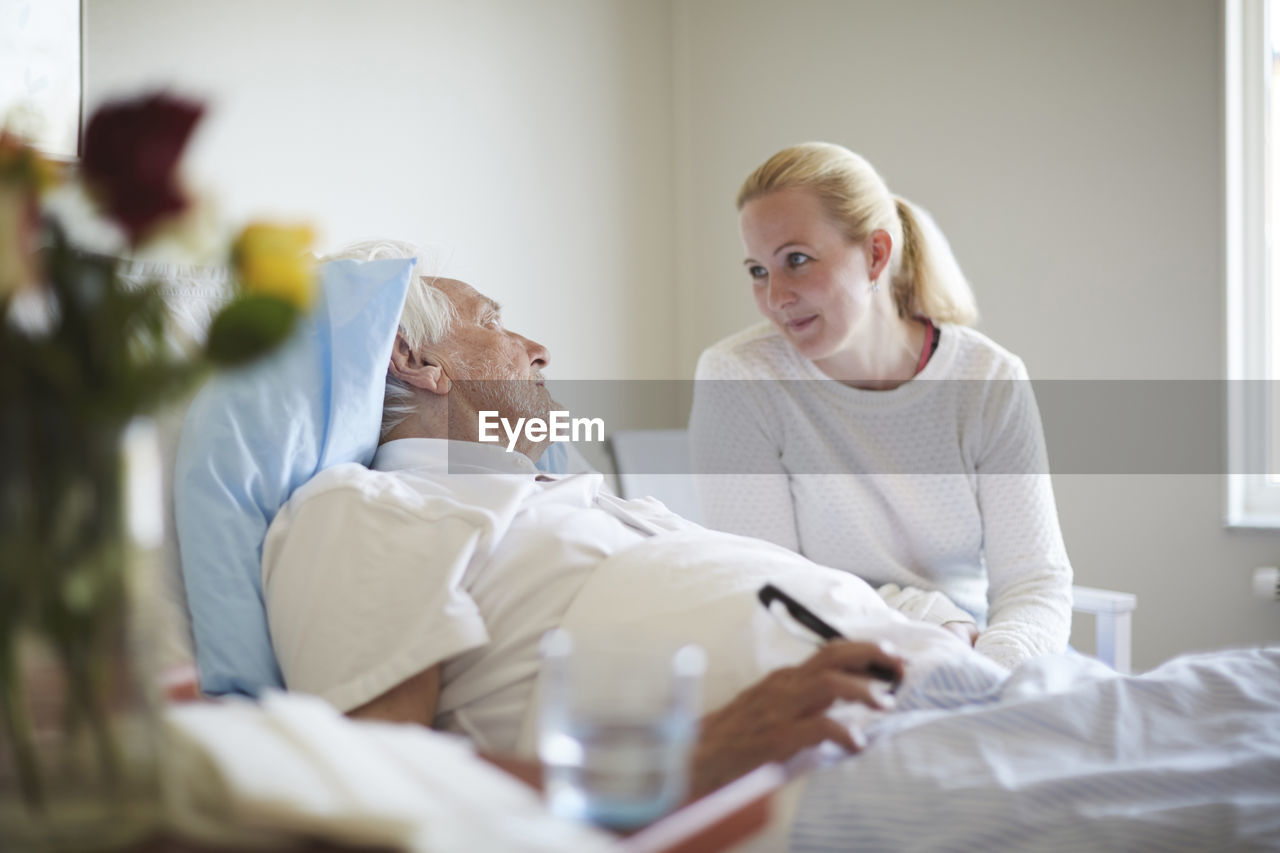 Daughter talking to senior man reclining on hospital bed