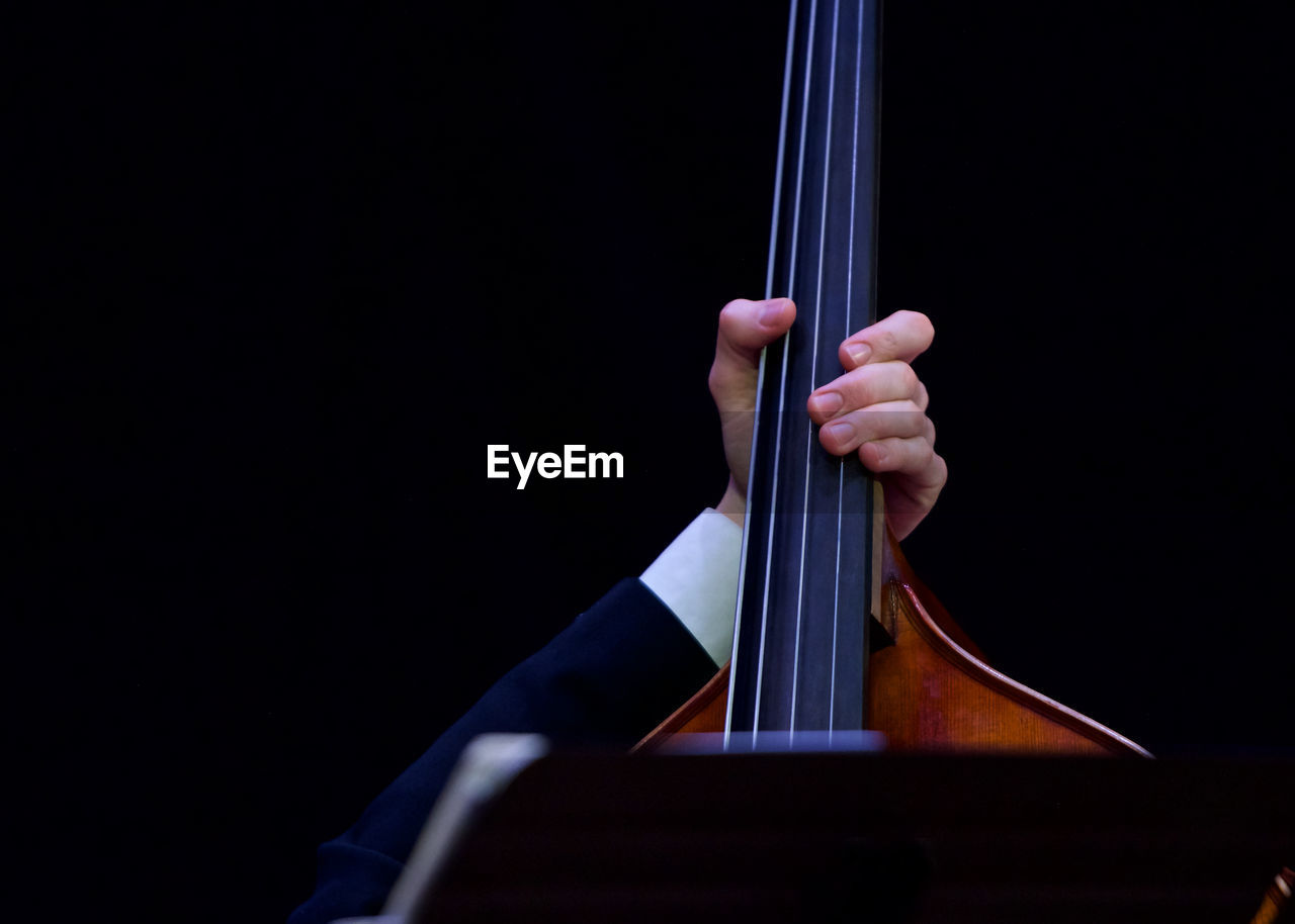 Cropped hand playing string instrument against black background