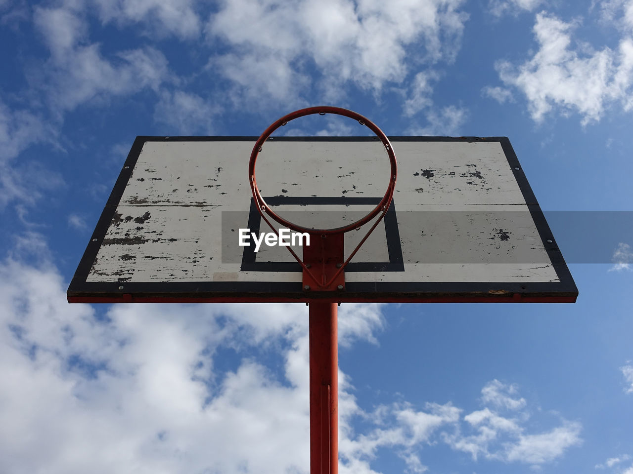 Basketball hoop on an outdoor court with sky and clouds background