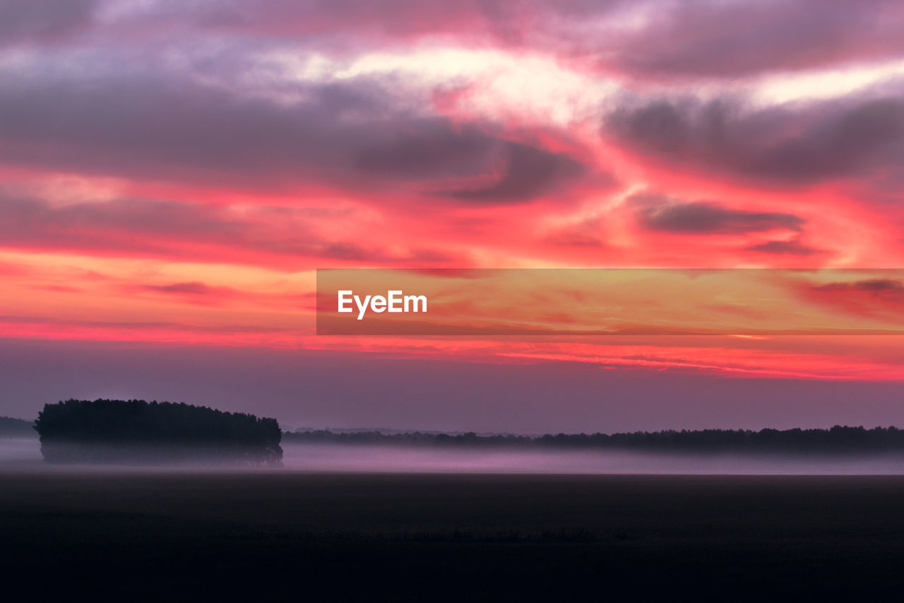 Scenic view of foggy field against orange sky during sunrise