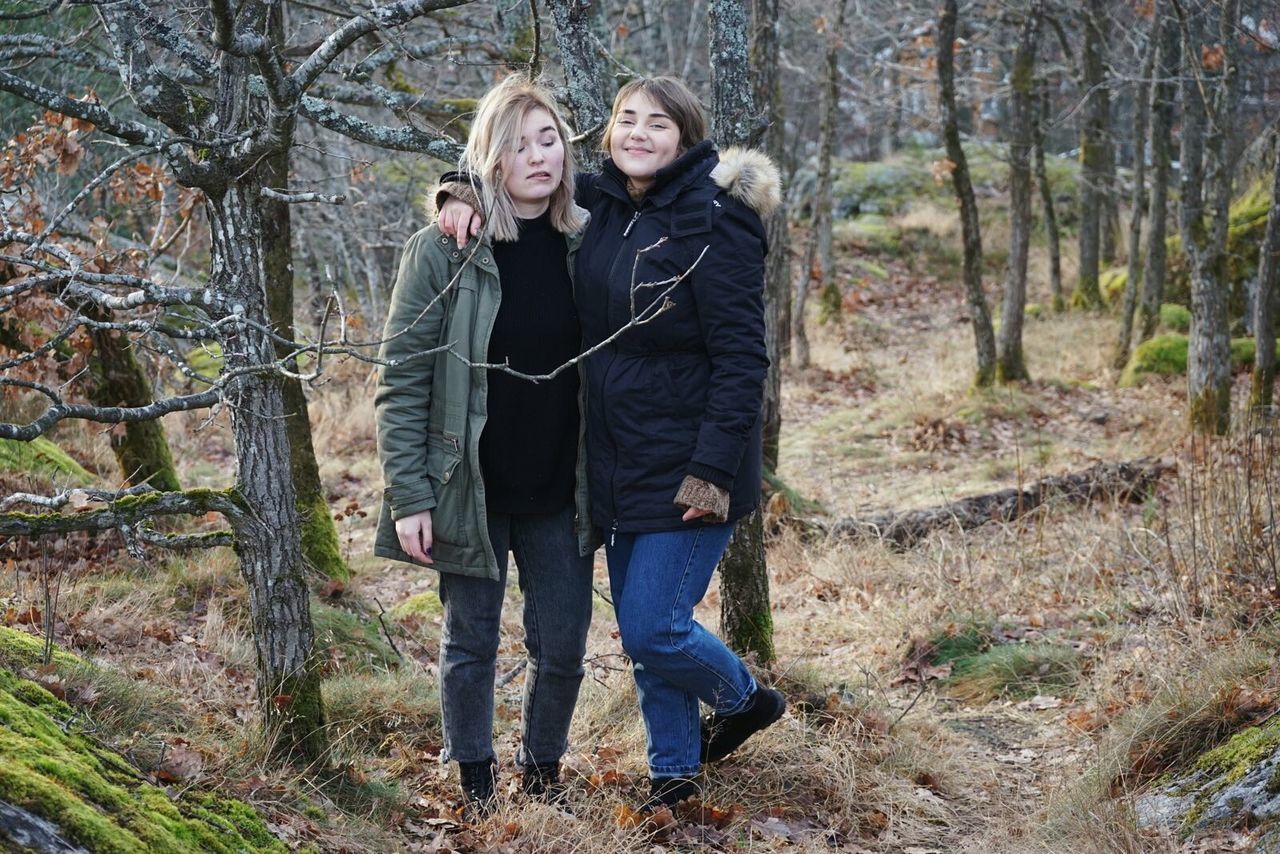 Full length friends standing against trees on field at forest