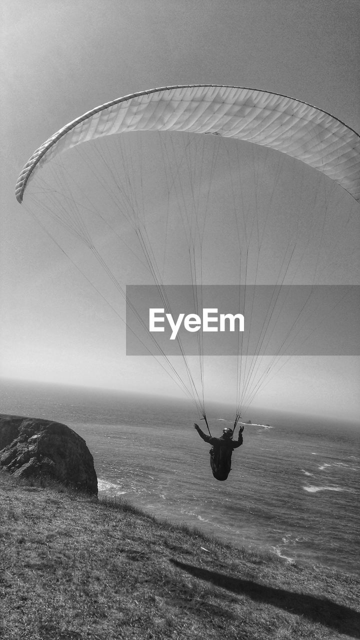 PERSON PARAGLIDING IN SEA AGAINST SKY