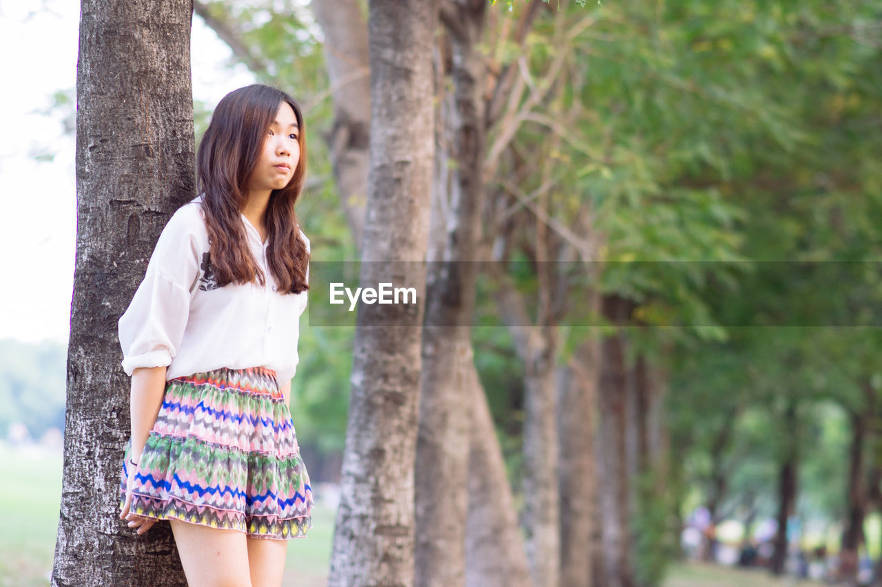 Young woman standing against tree trunk