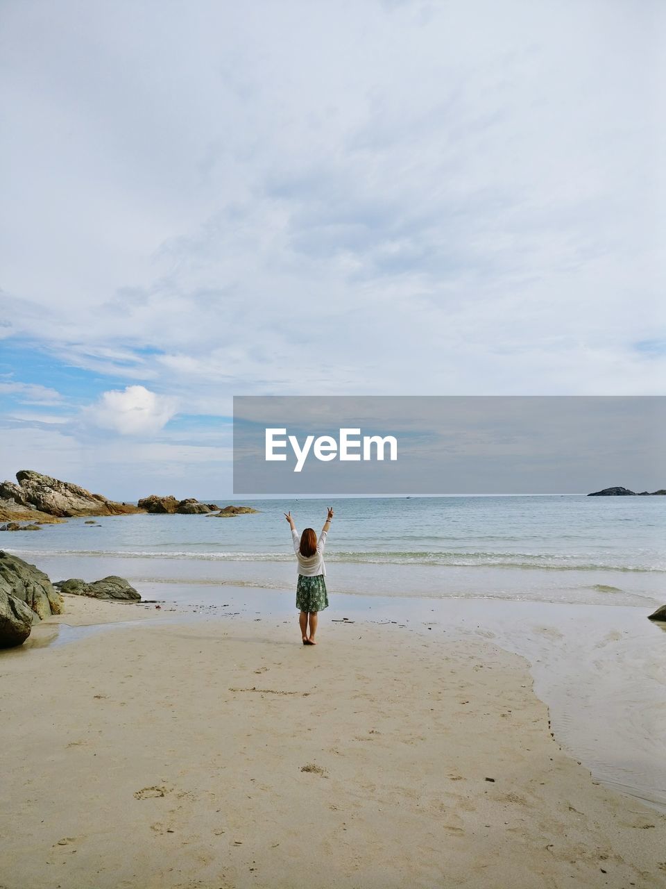 Rear view of woman standing on beach against sky