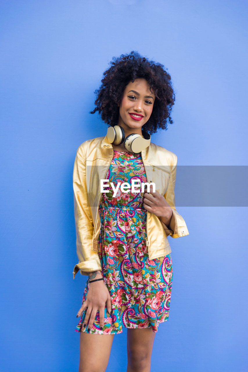 Fashionable young woman with curly hair against blue background