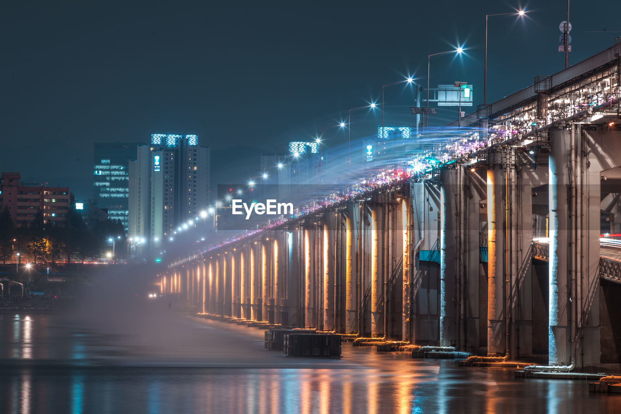 Illuminated bridge over river against sky in city at night