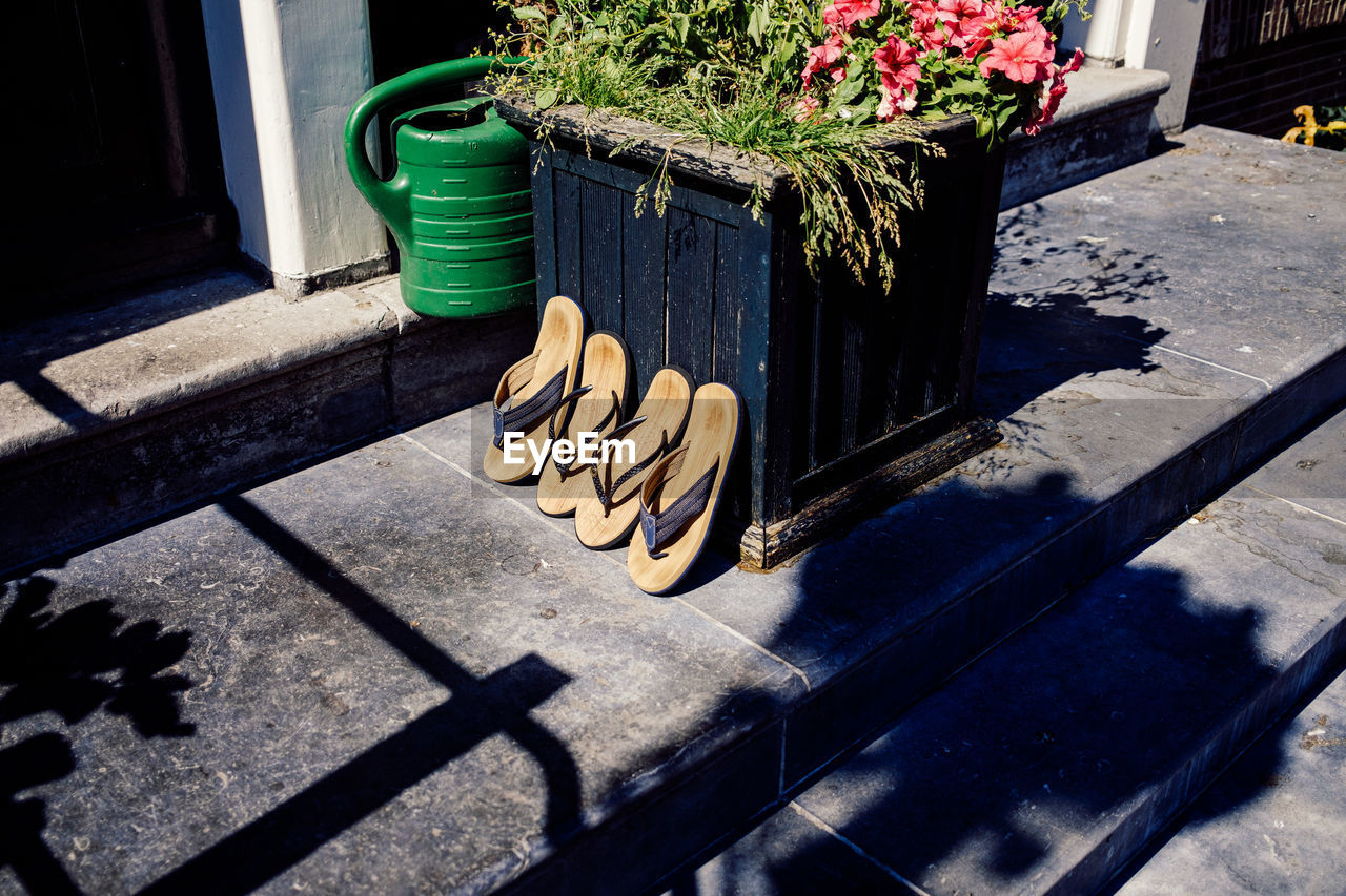 Four sandals leaning against a flower pot in the sunlight in front of a house entrance