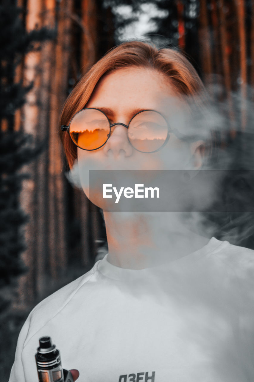 Close-up portrait of young woman exhaling smoke while standing in forest