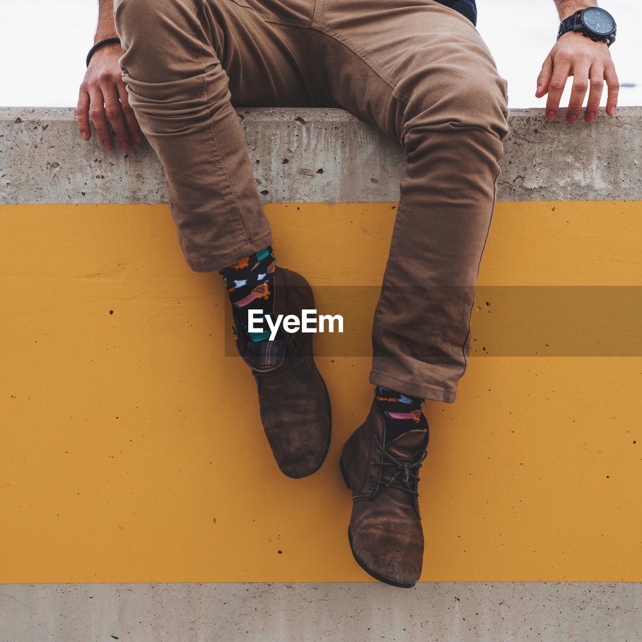 Low section of man sitting on orange retaining wall