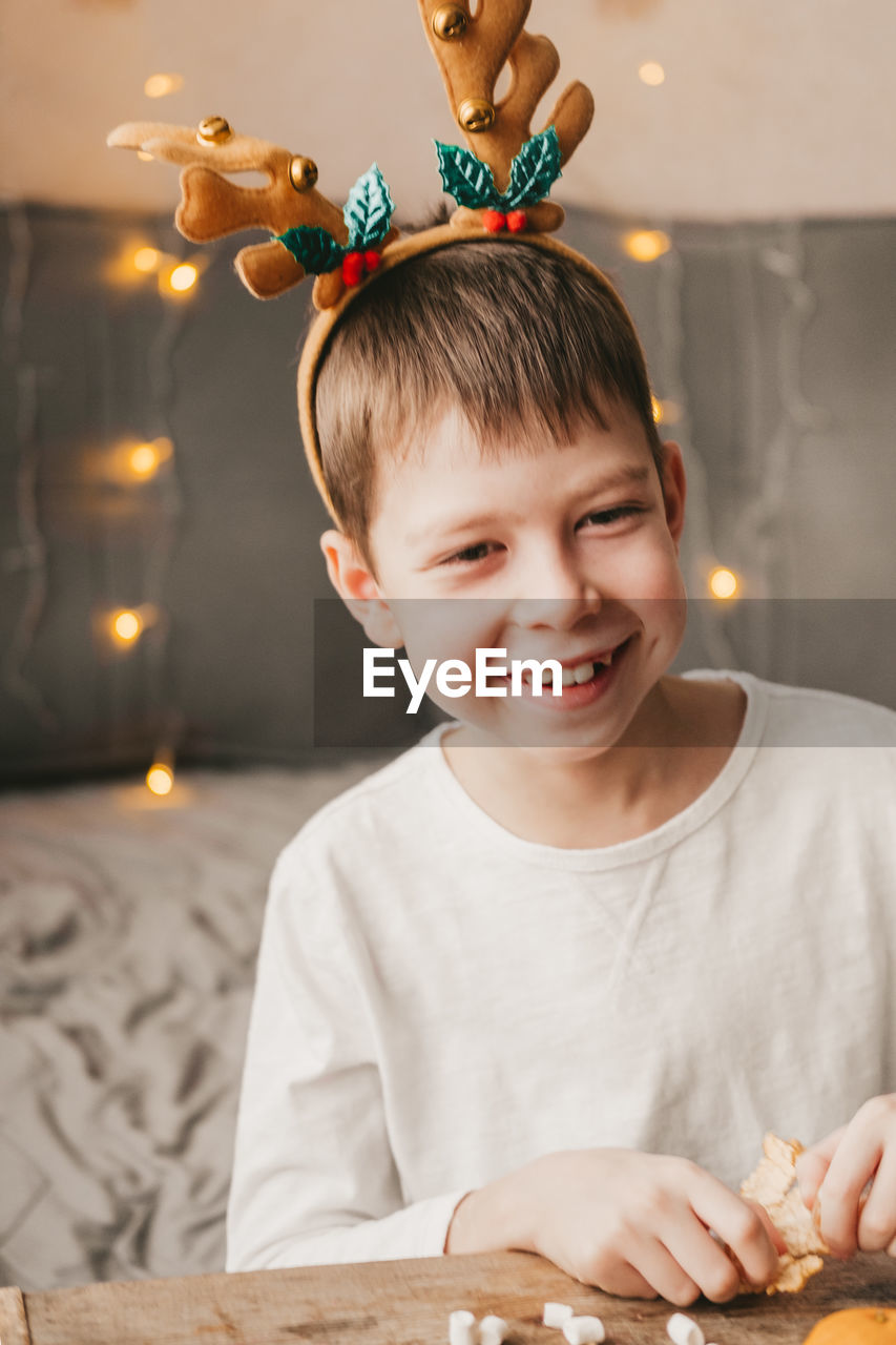 Portrait of a boy in reindeer christmas antlers on the background of an orange garland.