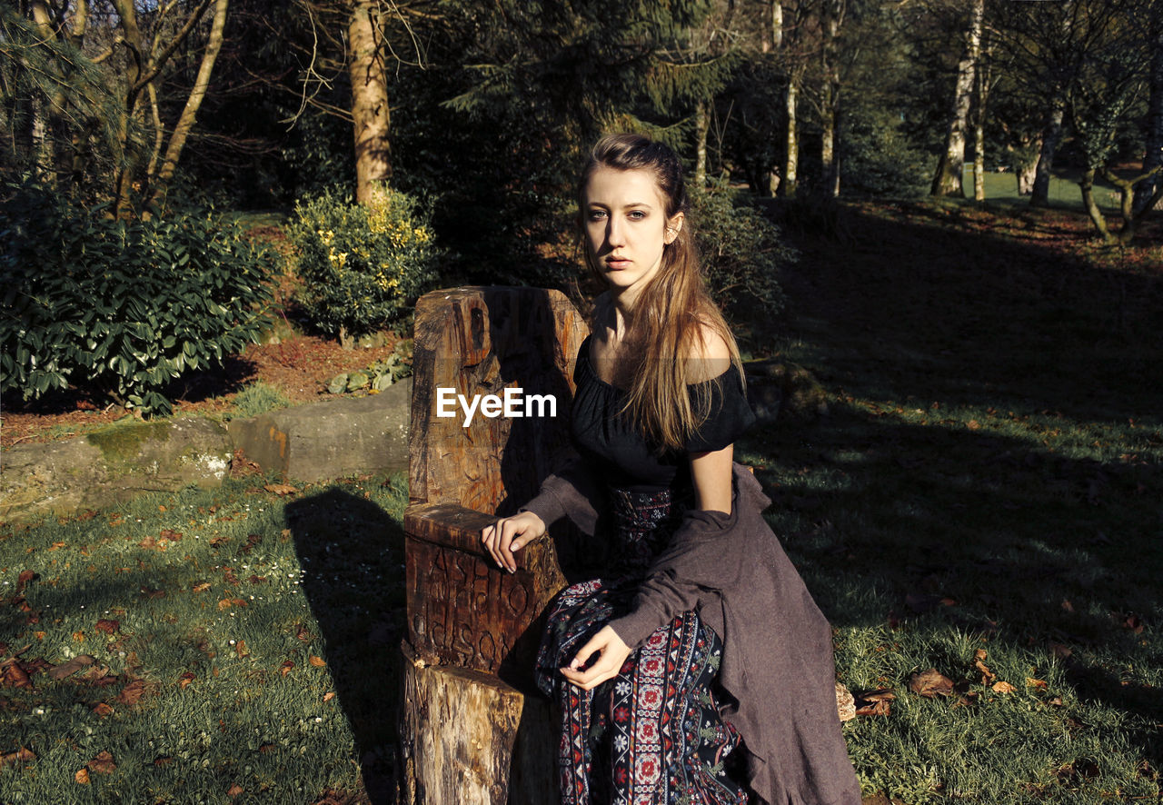 Portrait of young woman sitting on seat in forest