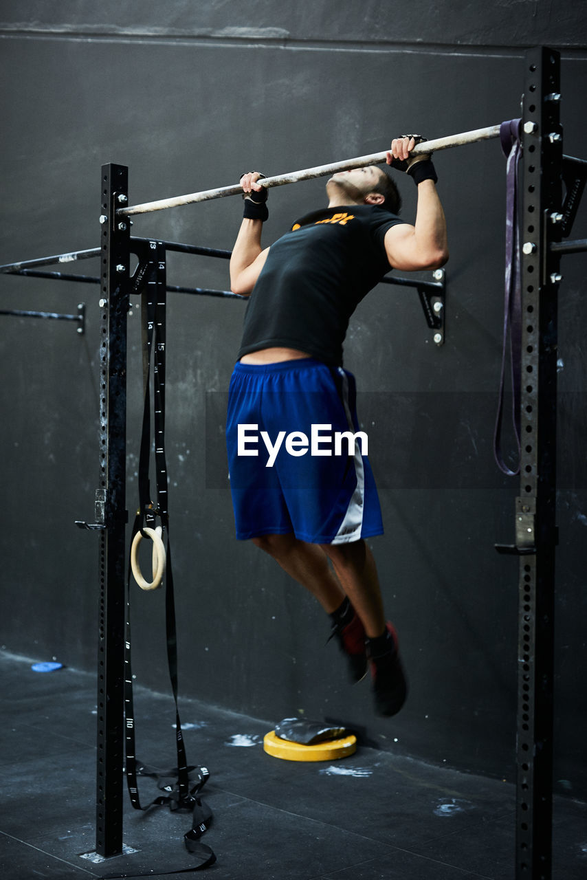 Young man working out doing chin ups in horizontal bar at indoors gym