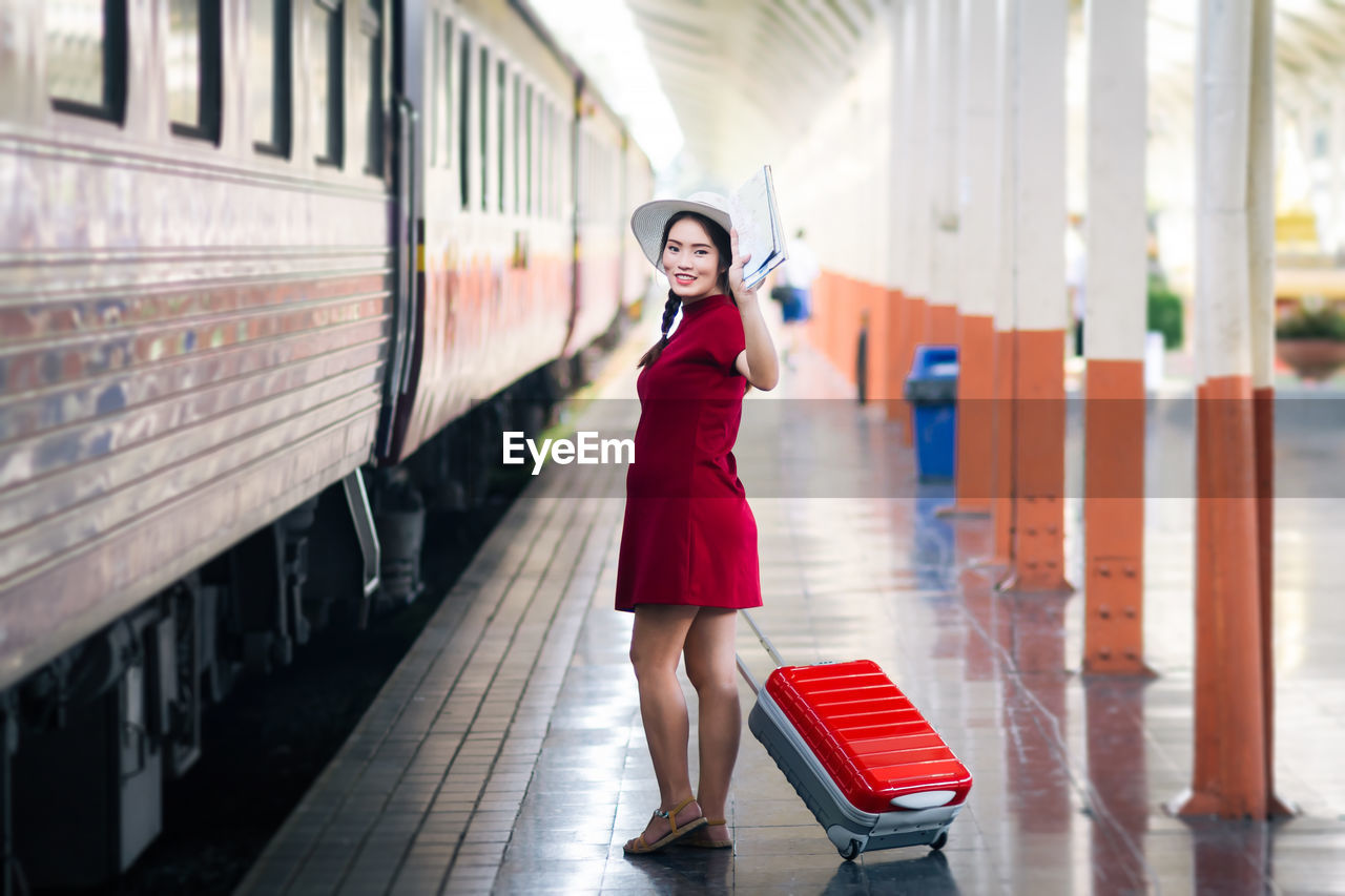 Portrait of smiling woman with suitcase walking by train at railroad station platform