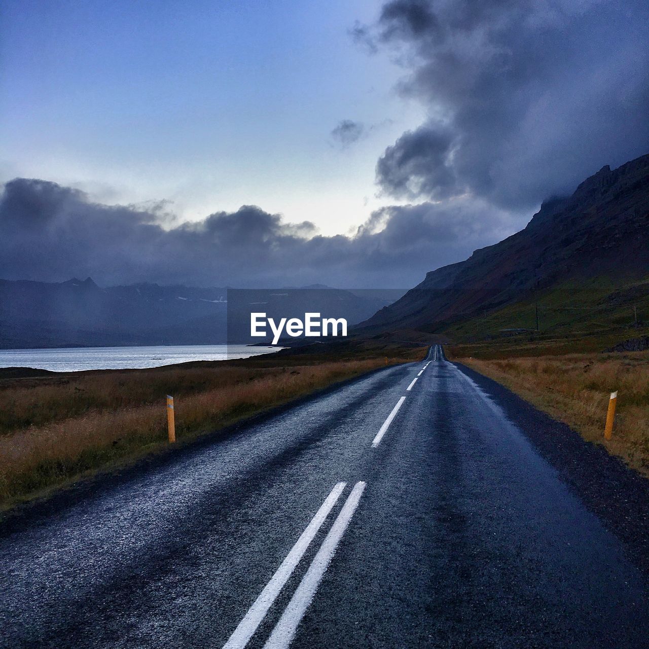 Icelandic road by mountain against cloudy sky at dusk