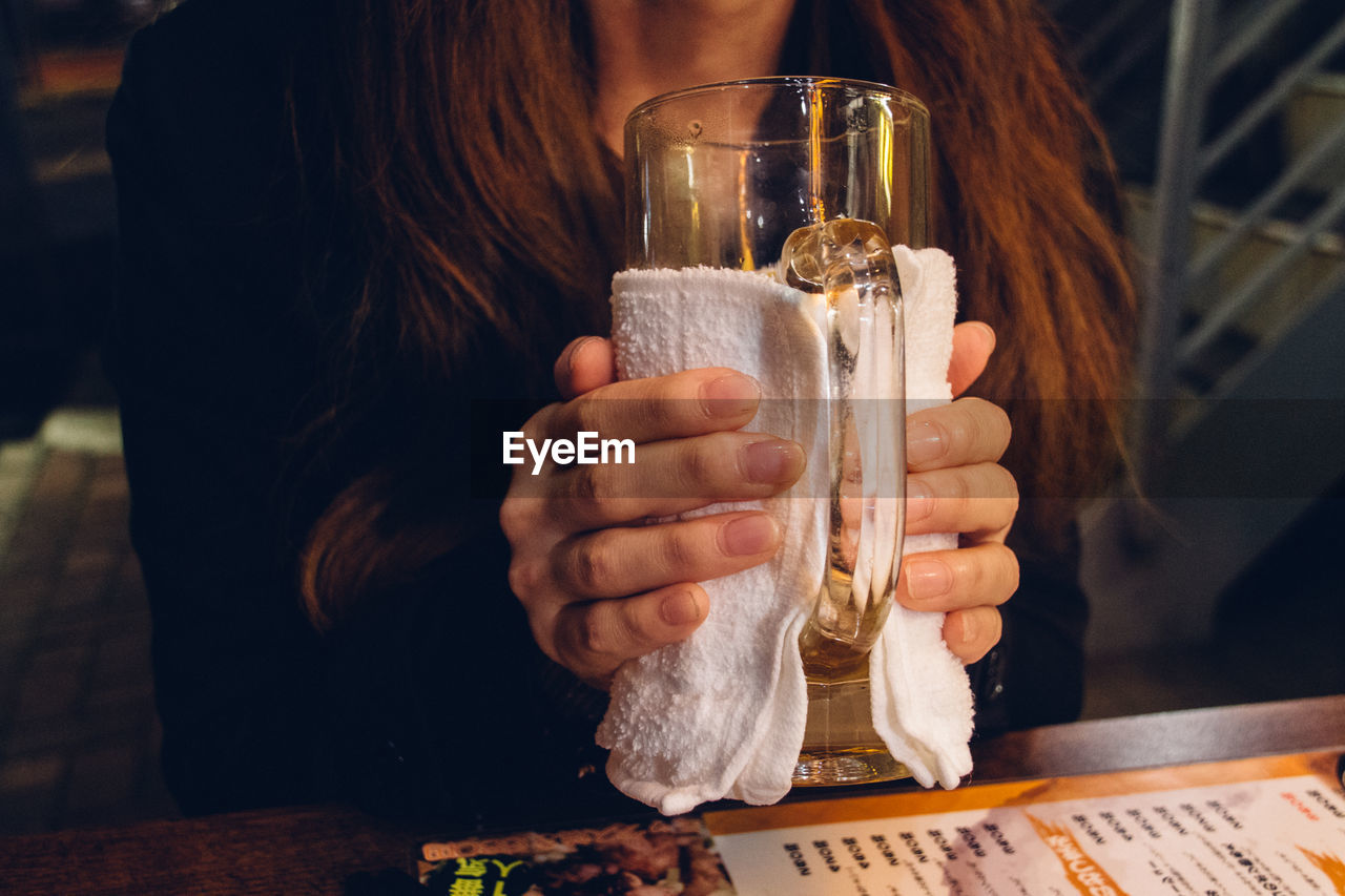 Midsection of woman holding glass at table in restaurant