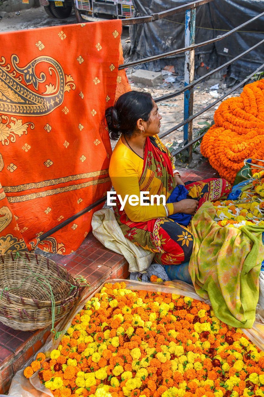 REAR VIEW OF MAN WITH ORANGE FLOWERS IN MARKET STALL