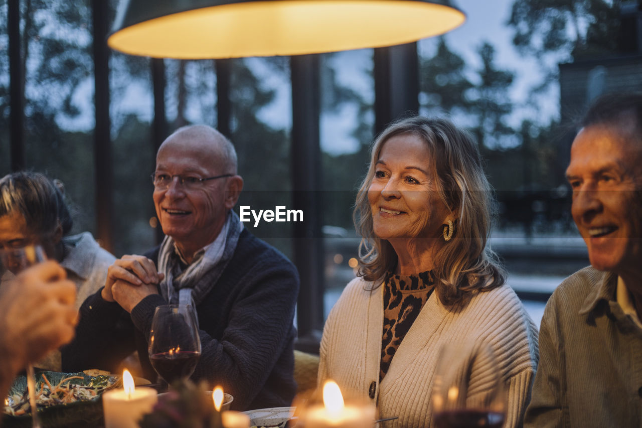 Smiling senior woman with male retired friends during dinner party