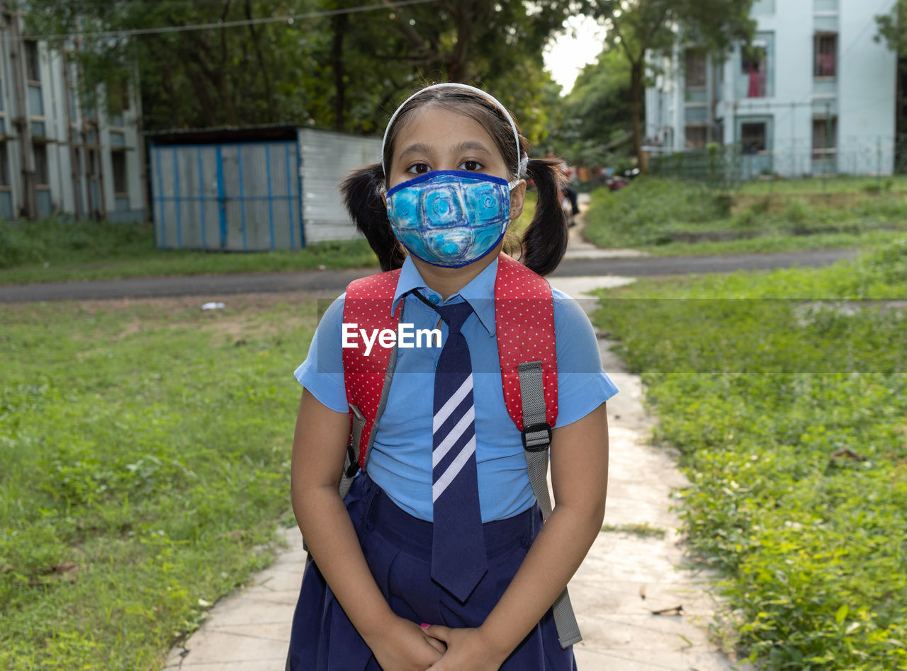 Portrait of a happy indian girl child student in school uniform nose mask protection going to school