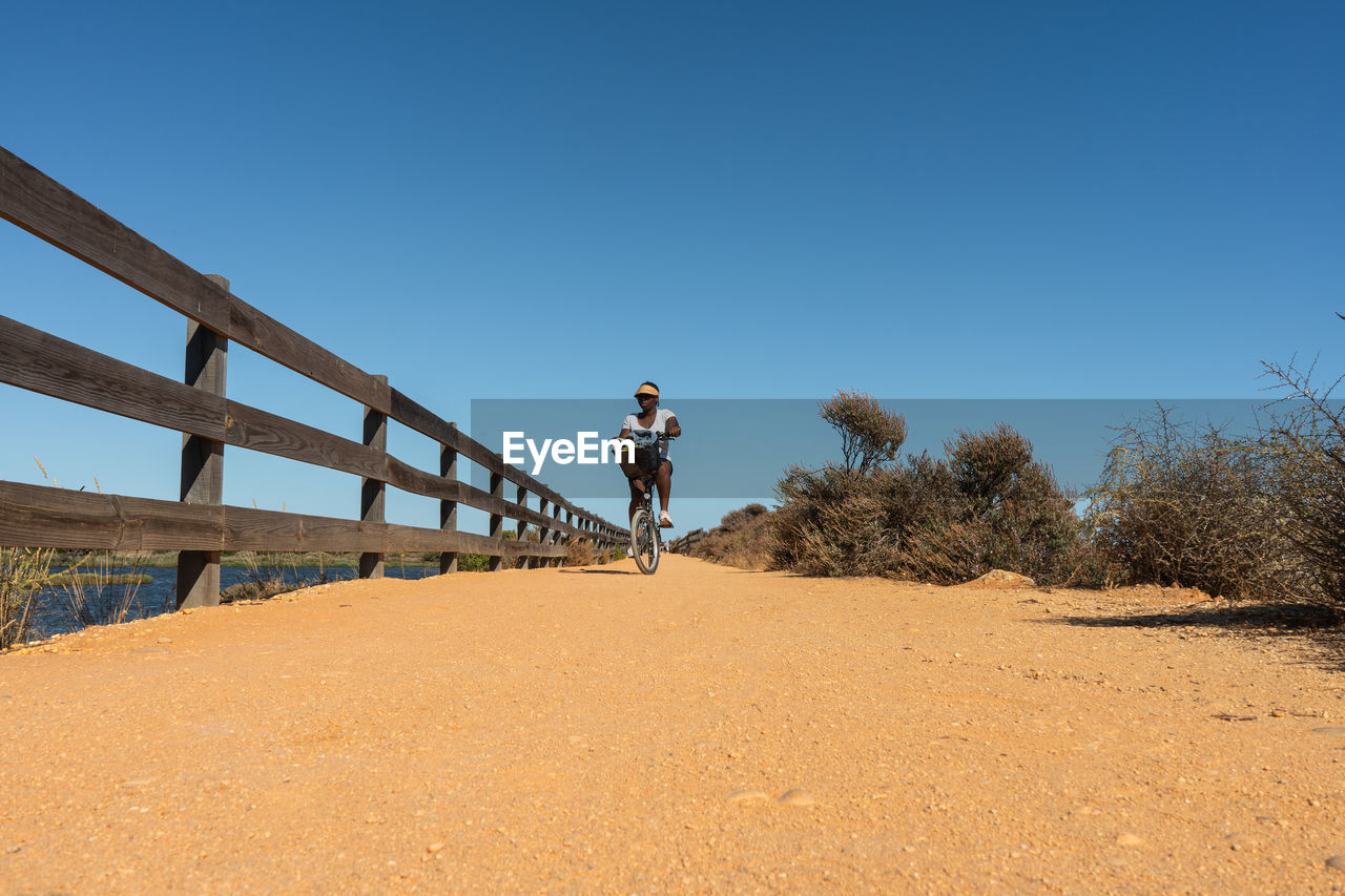 Black woman riding a bike on a sandy path in a sunny day