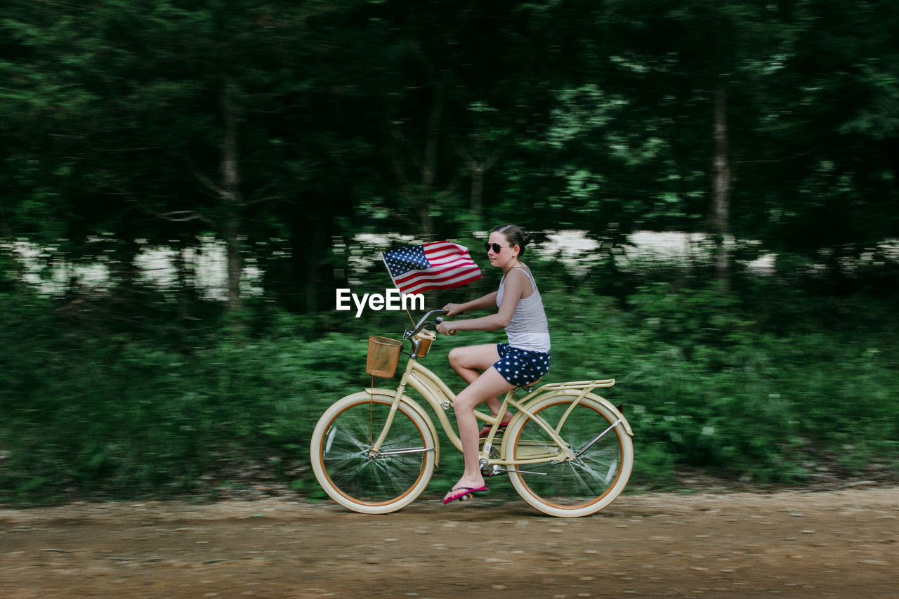 Girl riding her bike with an american flag on a rural dirt road