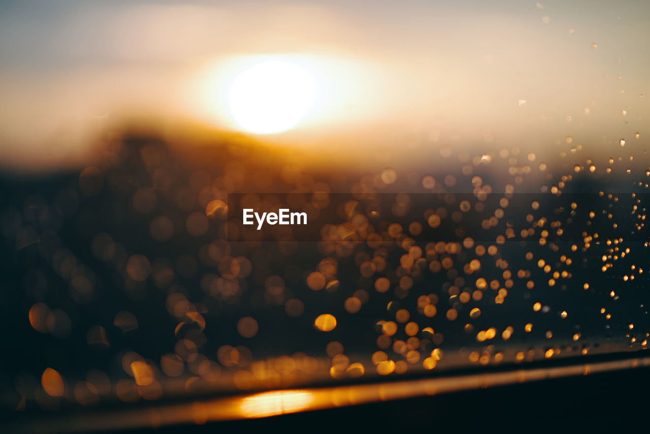 Defocused image of illuminated lights against sky during sunset